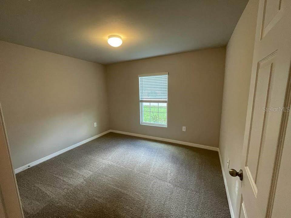 A carpeted bedroom with beige walls, a single window, and a white door — 456 MACARTHUR DRIVE, PORT CHARLOTTE, FL