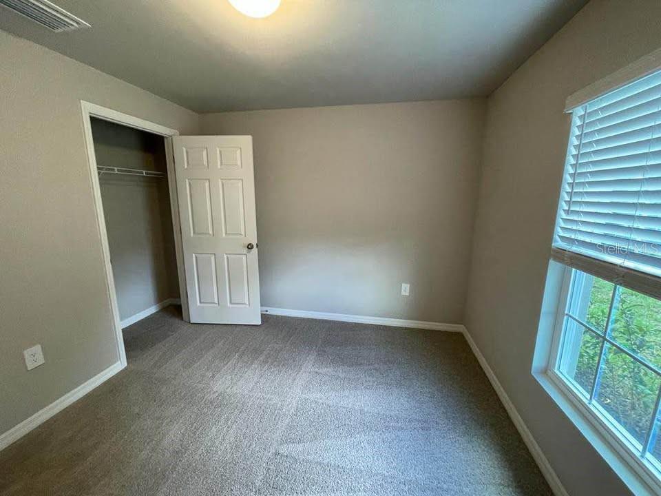 An empty bedroom features beige walls, gray carpeting, a white closet door, and a window — 456 MACARTHUR DRIVE, PORT CHARLOTTE, FL