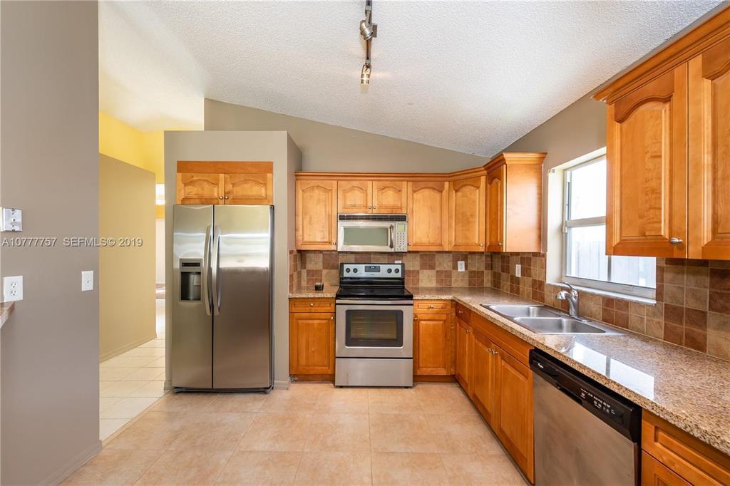 A kitchen features wood cabinets, stainless steel appliances, granite countertops, and a tiled backsplash — 6222 Flores Del Mar, Margate FL 33063, MARGATE, FL
