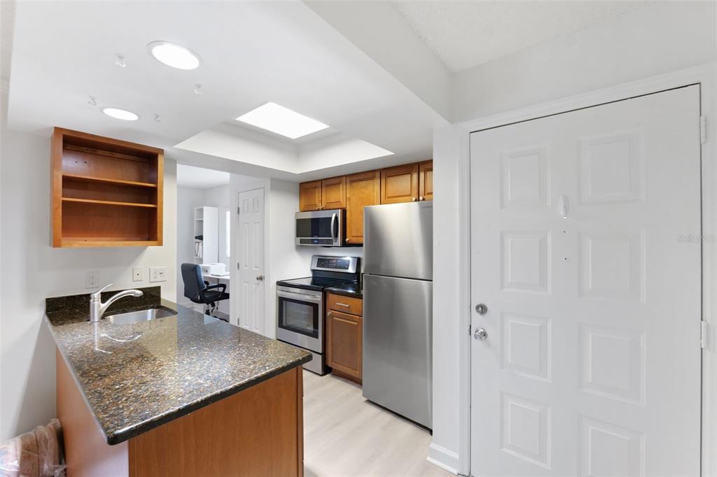 A kitchen features granite countertops, stainless steel appliances, wood cabinetry, and a white entry door — 3808 N OAK DRIVE UNIT U31, TAMPA, FL