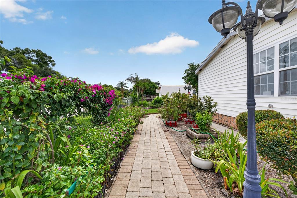A paved walkway leads past a flower-lined fence and a house exterior with a lamp post — 2558 MCINTOSH DRIVE, LAKELAND, FL