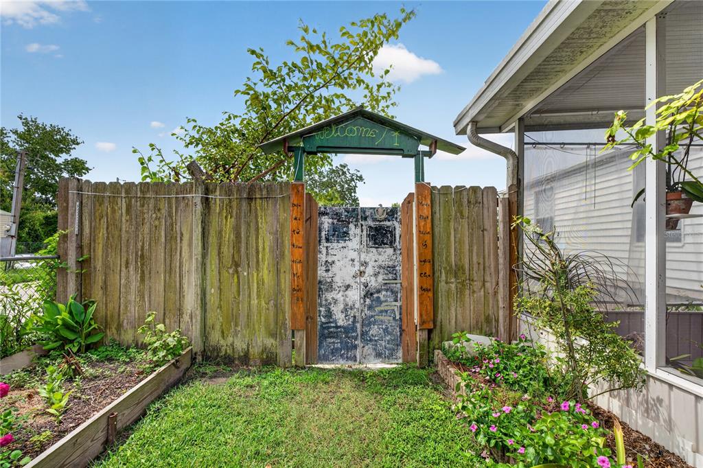 A weathered wooden fence features a central gate topped with a green welcome sign — 2558 MCINTOSH DRIVE, LAKELAND, FL