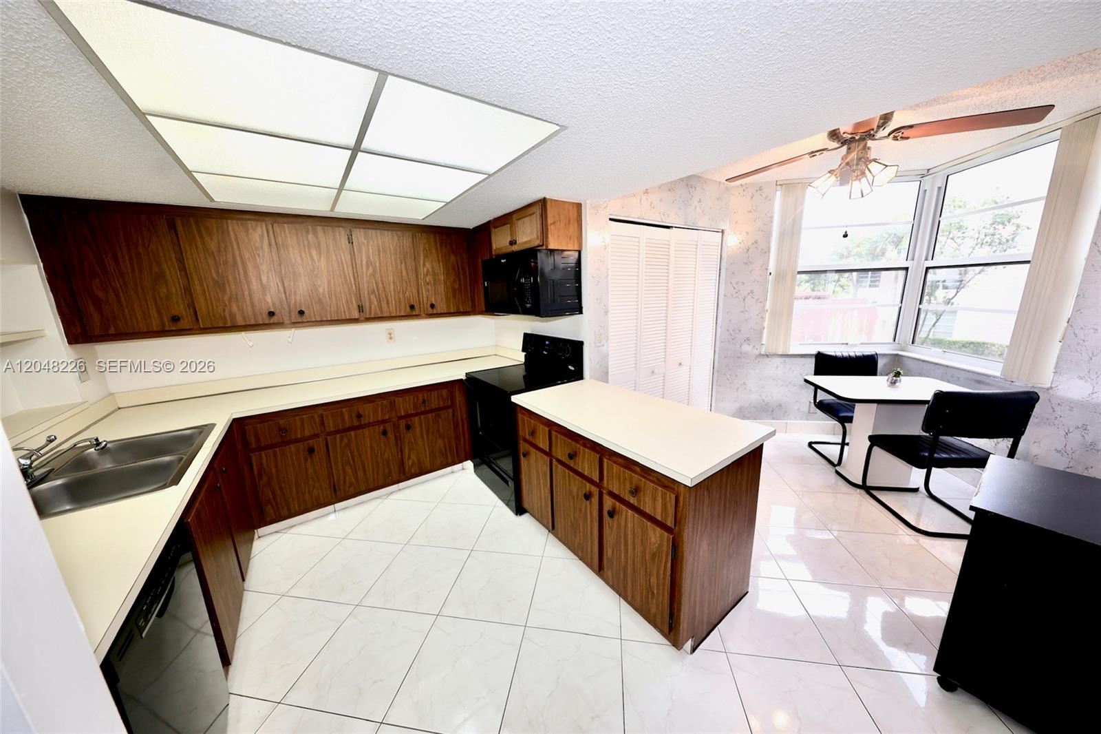 A kitchen features wood cabinets, white countertops, a tile floor, and a small dining area — 1831 Sabal Palm Dr # 208, Davie FL 33324, DAVIE, FL