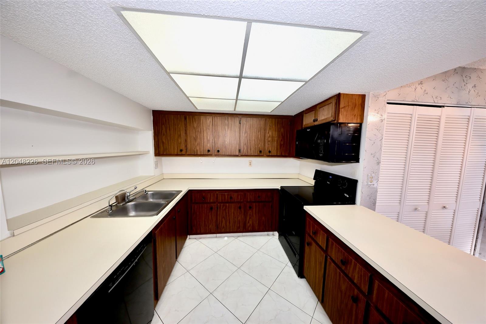 A kitchen features dark wood cabinets, white countertops, black appliances, and white tiled flooring — 1831 Sabal Palm Dr # 208, Davie FL 33324, DAVIE, FL