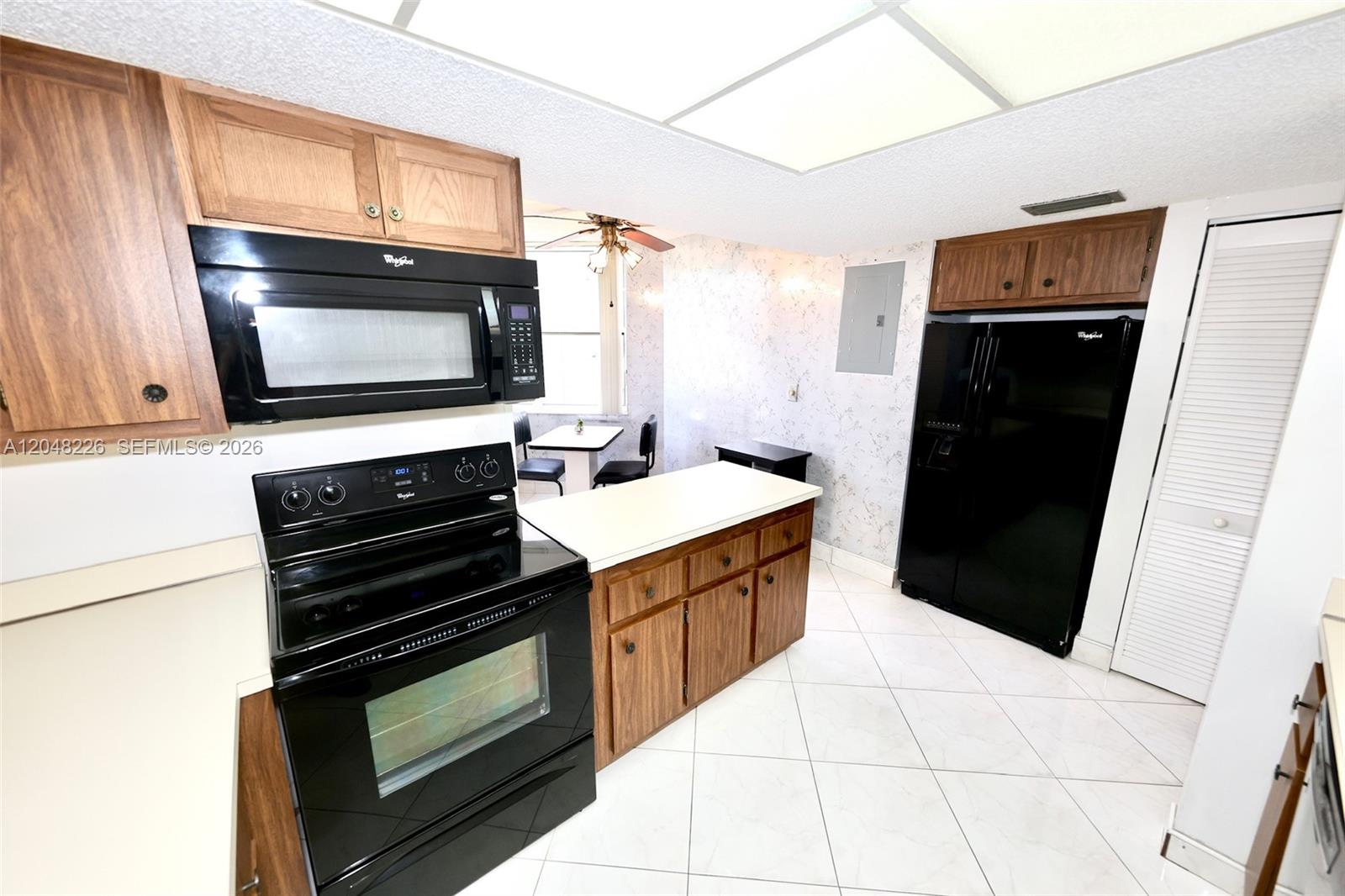 A kitchen features wood cabinets, black appliances, a white countertop, and white tiled flooring — 1831 Sabal Palm Dr # 208, Davie FL 33324, DAVIE, FL