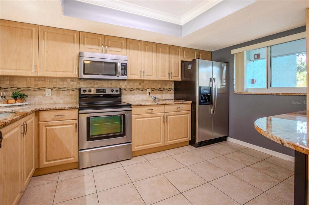 A kitchen with light wood cabinets, stainless steel appliances, granite countertops, and tiled flooring — 3300 BENEVA UNIT 214, SARASOTA, FL