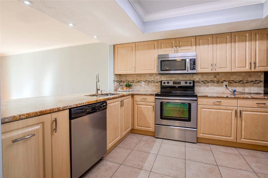 A kitchen features light wood cabinets, stainless steel appliances, and tan granite countertops — 3300 BENEVA UNIT 214, SARASOTA, FL