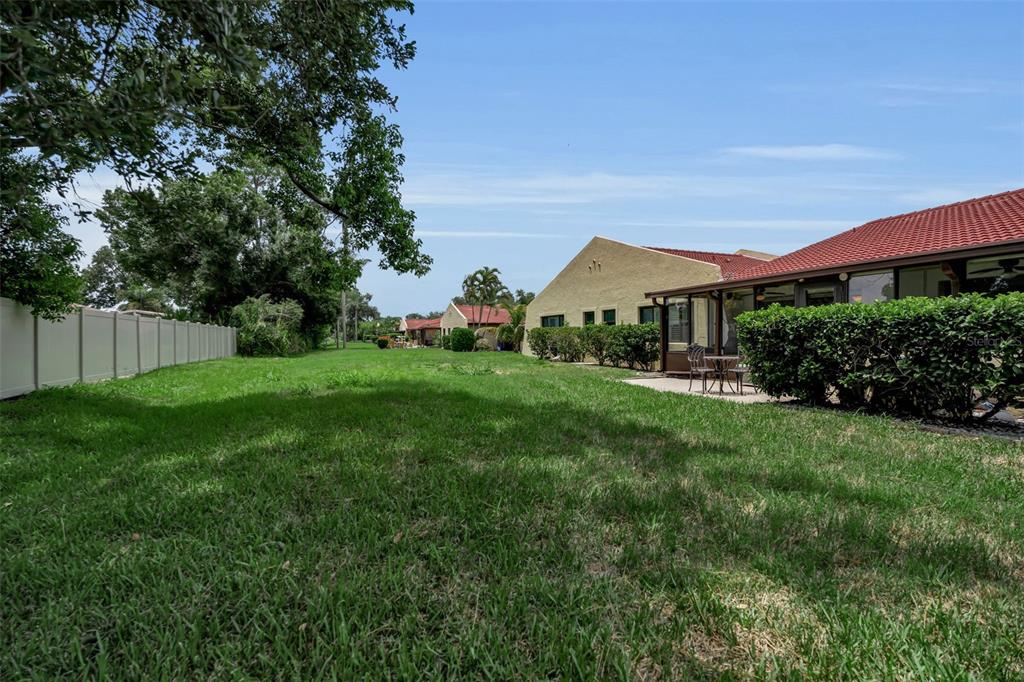 A grassy backyard area features a white fence, a patio, and several residential buildings — 1409 56TH STREET W UNIT 1409, BRADENTON, FL