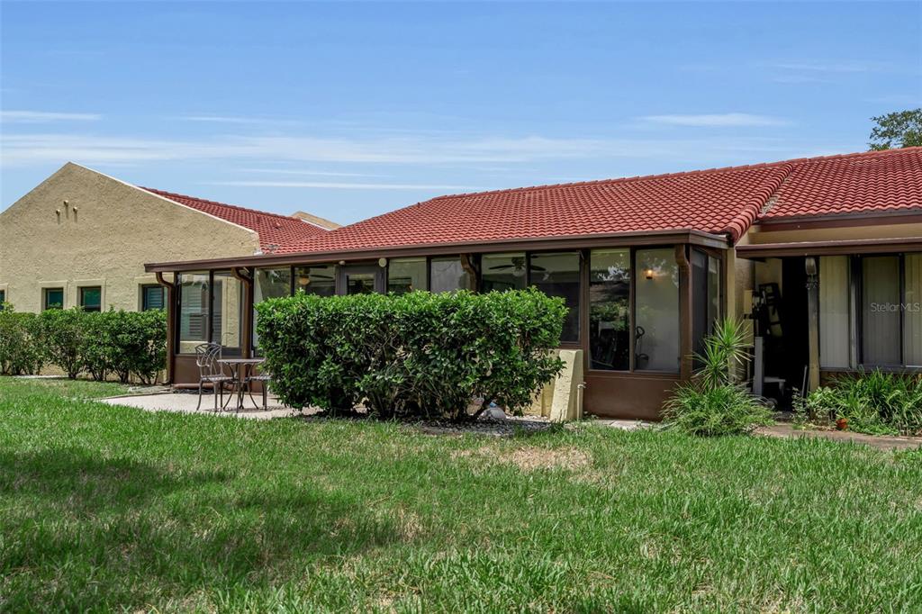 A backyard view of a house with a red tile roof and a screened-in porch — 1409 56TH STREET W UNIT 1409, BRADENTON, FL