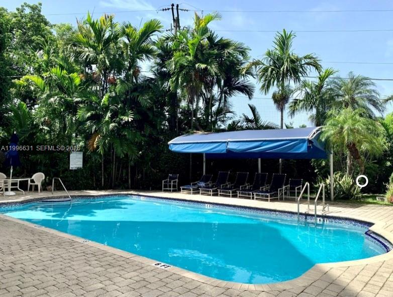 A swimming pool with a blue canopy and lounge chairs sits on a paved patio — BAY HARBOR ISLANDS, FL