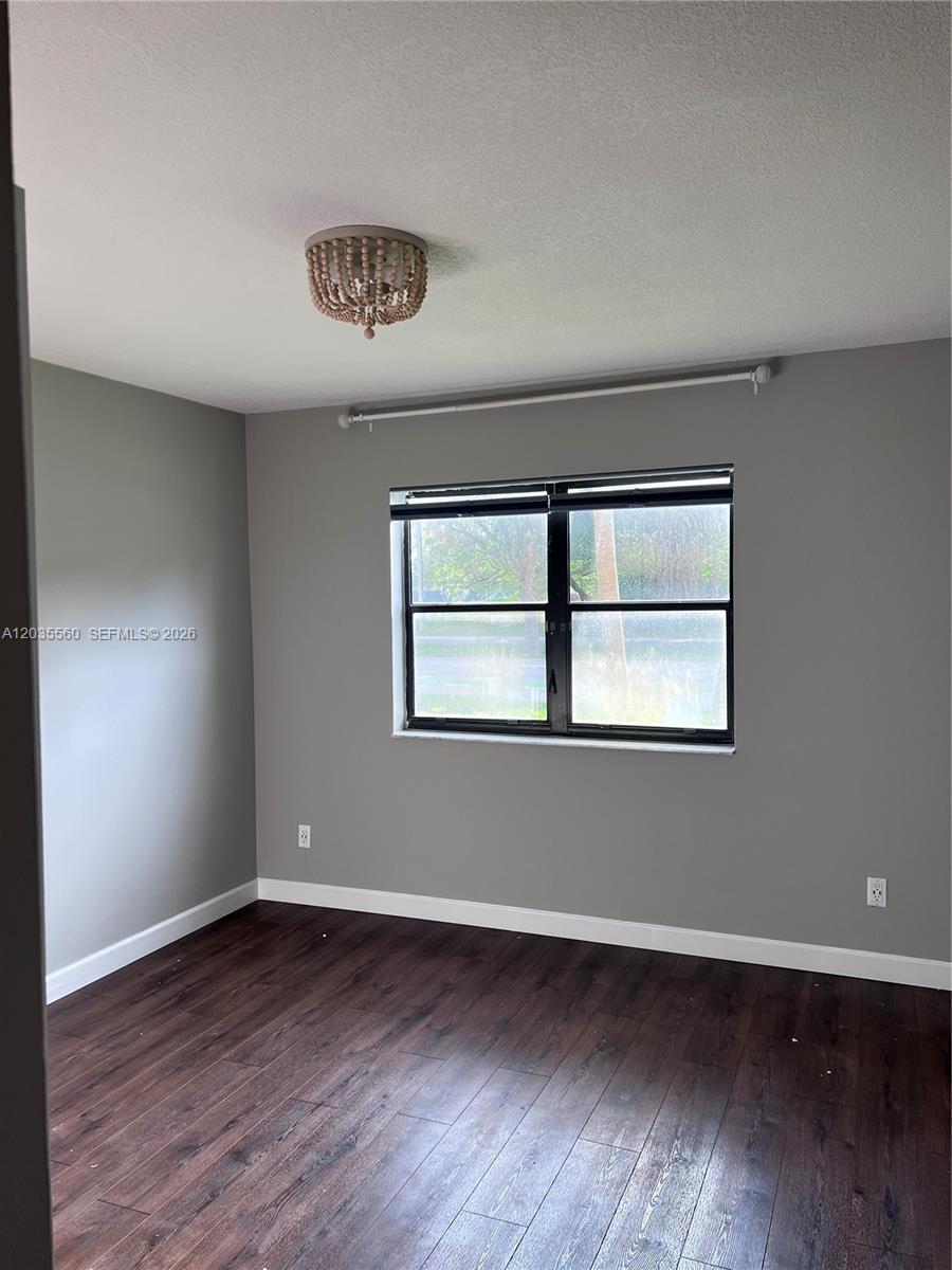 A bedroom features gray walls, dark wood-look flooring, a beaded light fixture, and a window — HOLLYWOOD, FL