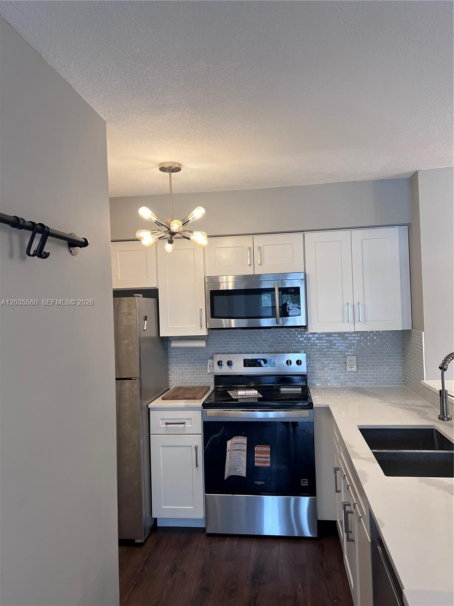A kitchen features white cabinets, stainless steel appliances, a light-colored backsplash, and a modern chandelier — HOLLYWOOD, FL