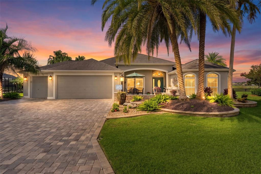 A single-story house with a paved driveway, palm trees, and a landscaped front yard at sunset — 3676 VINELAND AVENUE, THE VILLAGES, FL
