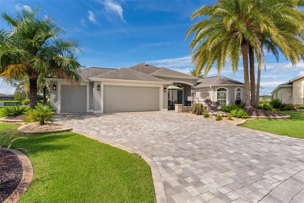 A single-story house with a paved driveway, three-car garage, and palm trees under a blue sky — 3676 VINELAND AVENUE, THE VILLAGES, FL