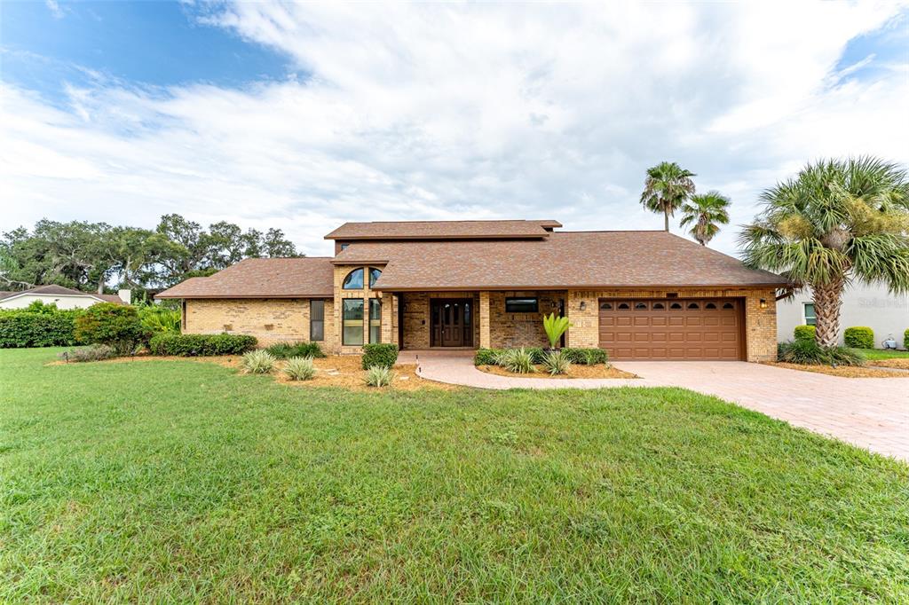 A single-story brick house with a brown shingled roof, a two-car garage, and palm trees — 6151 SILVER OAKS DRIVE, ZEPHYRHILLS, FL