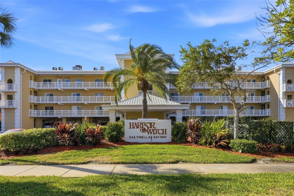 A multi-story yellow apartment building with white balconies stands behind a landscaped entrance sign — 544 PINELLAS BAYWAY S UNIT TH13, TIERRA VERDE, FL