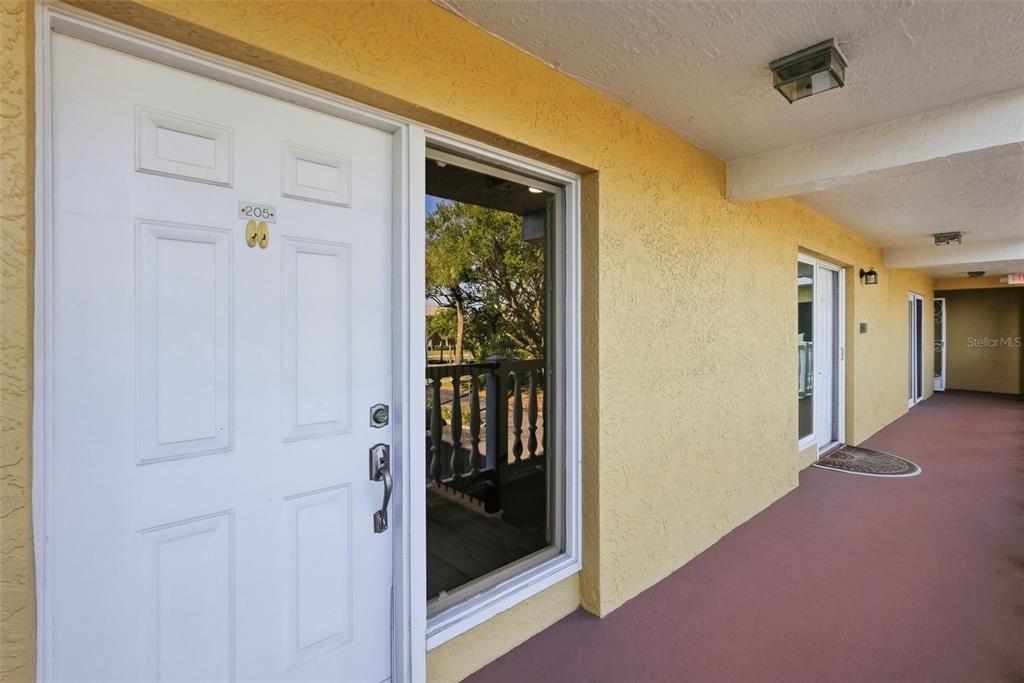 A white front door labeled 205 opens onto a covered outdoor walkway with yellow walls — 544 PINELLAS BAYWAY S UNIT TH13, TIERRA VERDE, FL