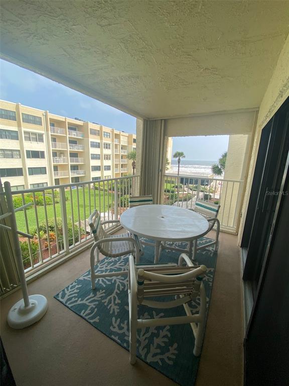 A balcony with a round table, chairs, and a patterned rug overlooking the ocean — 4175 S ATLANTIC AVENUE UNIT 3160, NEW SMYRNA BEACH, FL