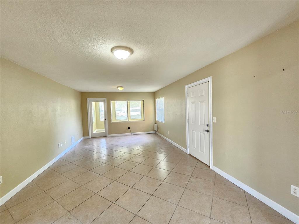 An empty room with beige walls, tile flooring, two ceiling lights, and a white door — 1365 DREW STREET UNIT 102, CLEARWATER, FL