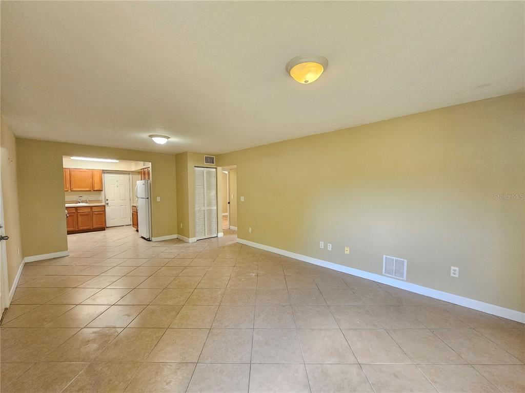 An open-concept living area with beige walls, tile flooring, and an adjacent kitchen — 1365 DREW STREET UNIT 102, CLEARWATER, FL