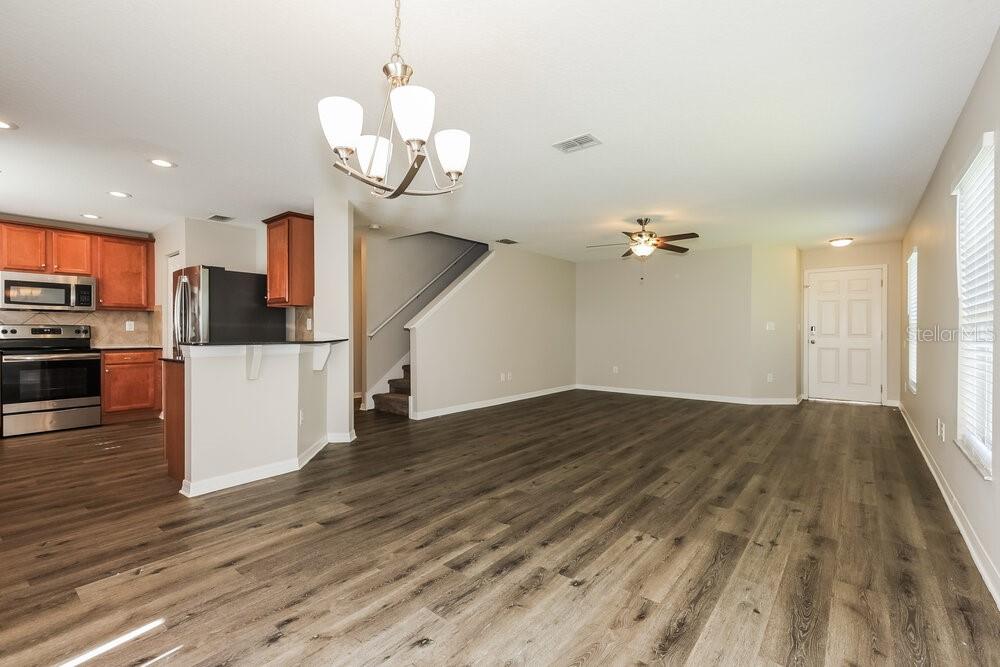 An open-concept living area features wood-look flooring, a kitchen with stainless appliances, and a staircase — 9540 SIMEON DRIVE, LAND O LAKES, FL