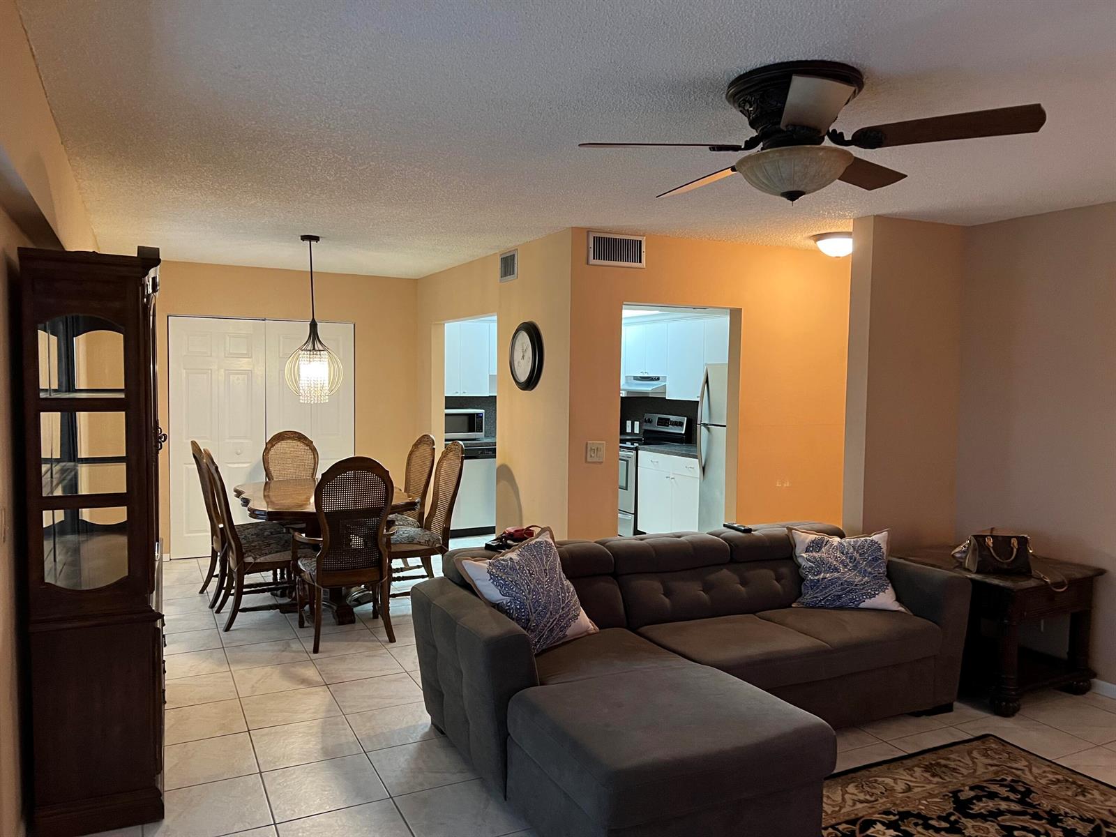 An open-concept living and dining area features tile flooring, a grey sectional, and kitchen views — 203 Suffolk, Boca Raton FL 33434, BOCA RATON, FL