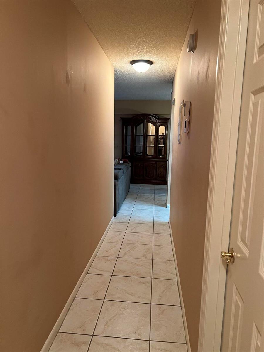 A hallway with beige walls and light-colored tile flooring leads toward a dining room — 203 Suffolk, Boca Raton FL 33434, BOCA RATON, FL