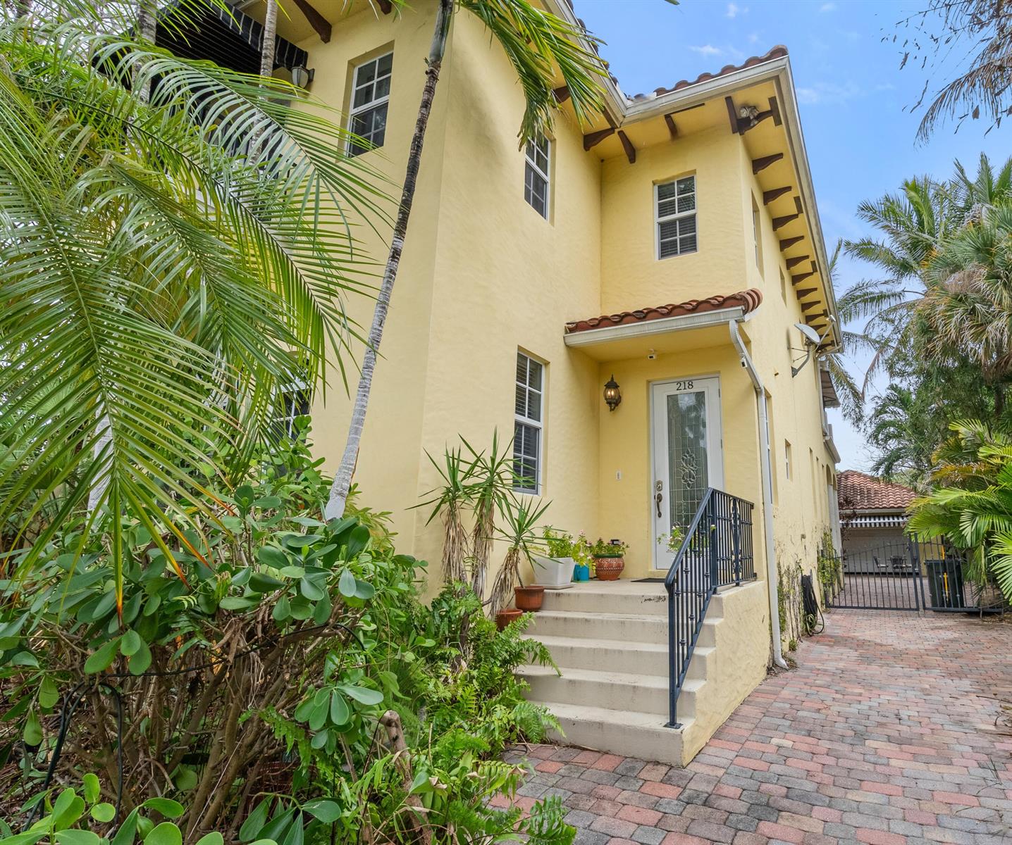 A yellow two-story house with a brick driveway, front steps, and lush tropical landscaping — 218 N Palmway, FL 33460, FL