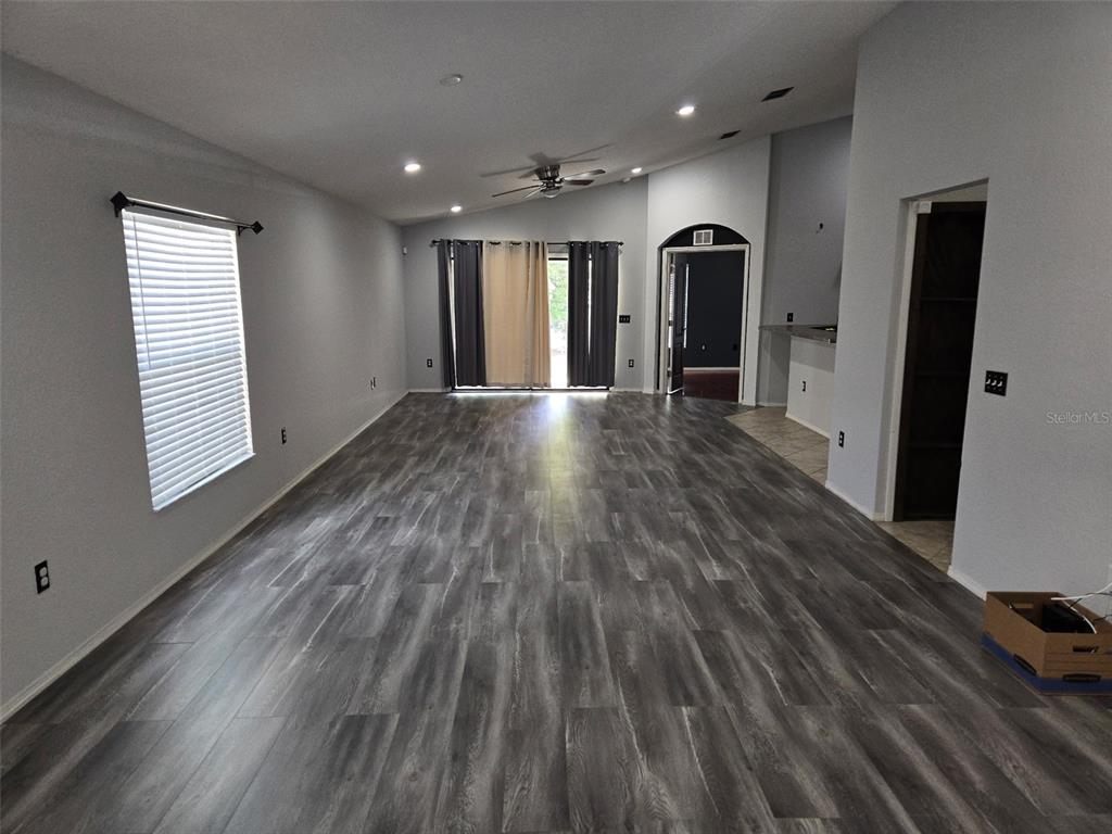 A spacious living room features gray wood-look flooring, vaulted ceilings, and sliding glass patio doors — 2235 LAKERIDGE DRIVE, WINTER HAVEN, FL