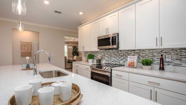 A modern kitchen features white cabinets, quartz countertops, a stainless steel sink, and tile backsplash — TBD SW 31ST TERRACE ROAD, OCALA, FL