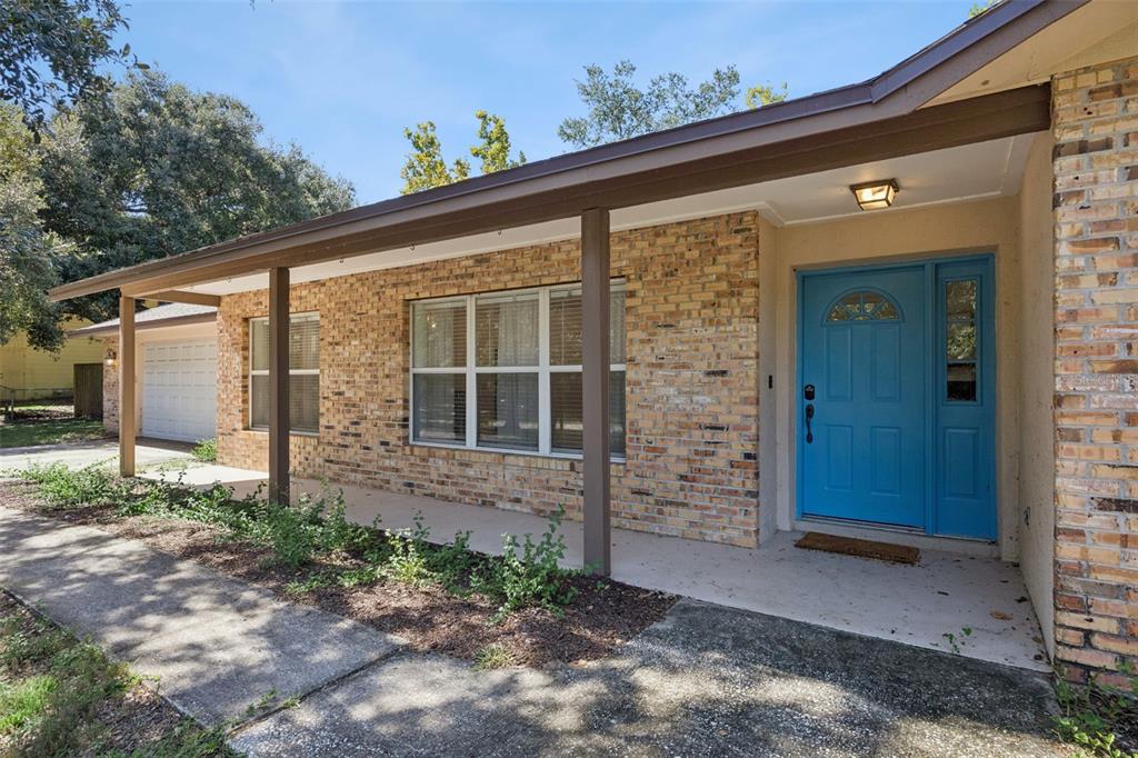 A brick house exterior features a covered porch, a bright blue front door, and windows — 16045 HARBAR OAKS DRIVE, MONTVERDE, FL