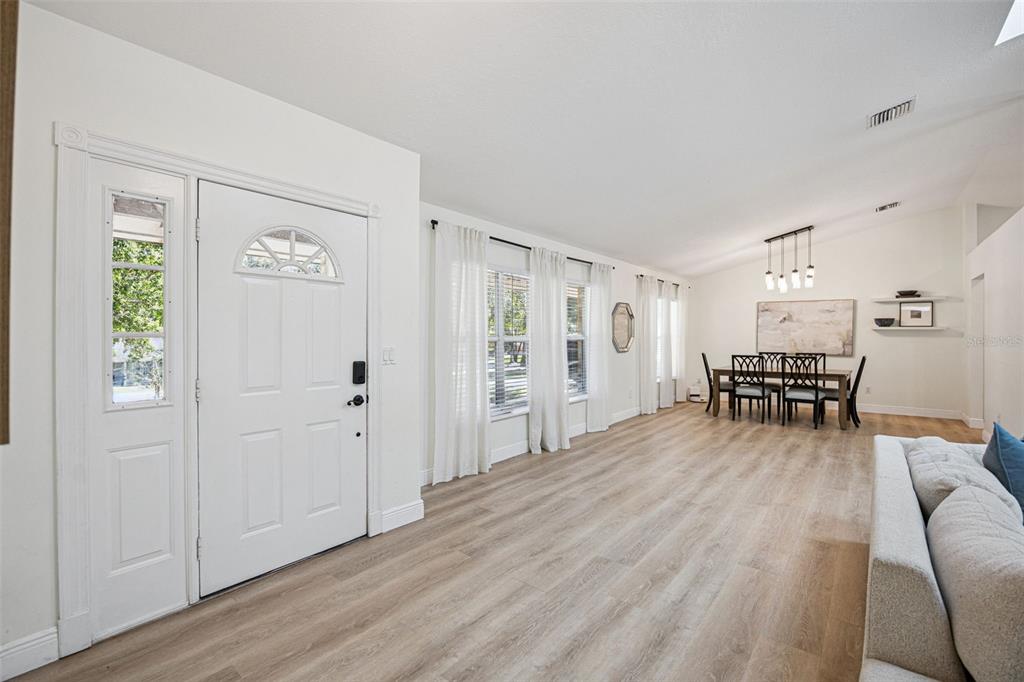 A bright, open-concept living and dining area features light wood flooring and a white front door — 16045 HARBAR OAKS DRIVE, MONTVERDE, FL