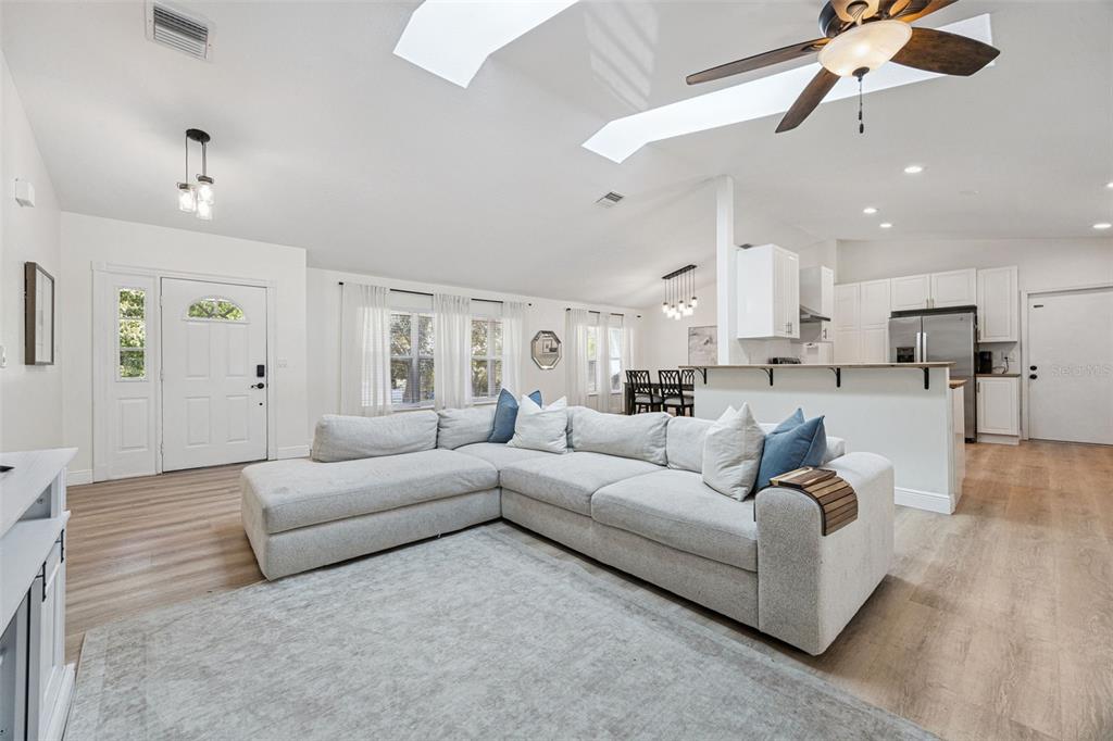 A bright, open-concept living room features a large sectional sofa, vaulted ceilings, and white cabinetry — 16045 HARBAR OAKS DRIVE, MONTVERDE, FL