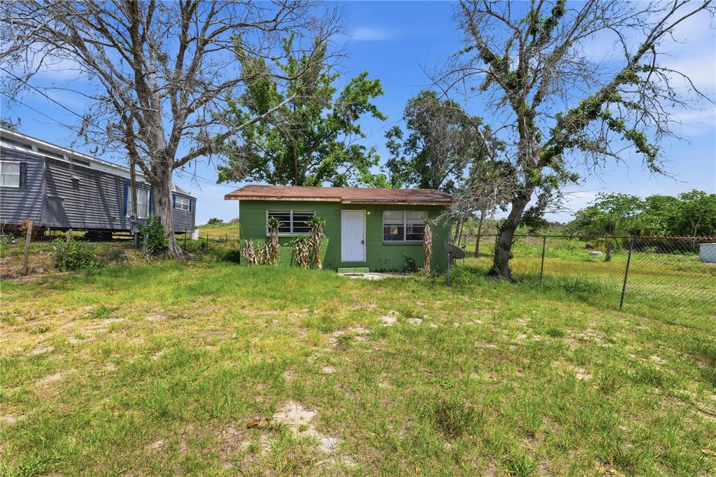 A small green house with a white door stands in a grassy yard with trees — 4610 WEEPING WILLOW AVENUE, SEBRING, FL