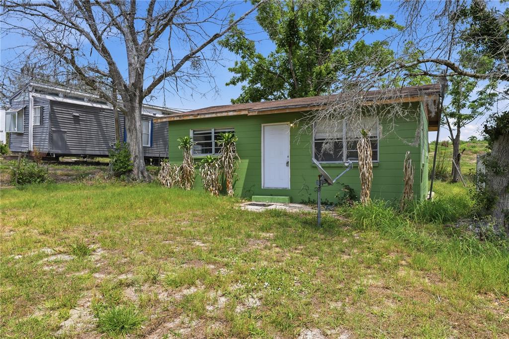 A small green house with a white door sits on a grassy lot near a trailer — 4610 WEEPING WILLOW AVENUE, SEBRING, FL