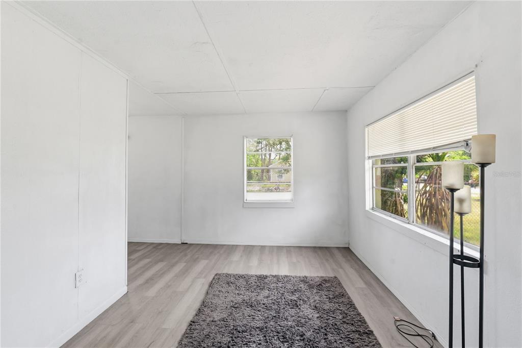 An empty room with white walls, light wood-look flooring, a gray rug, and two windows — 4610 WEEPING WILLOW AVENUE, SEBRING, FL