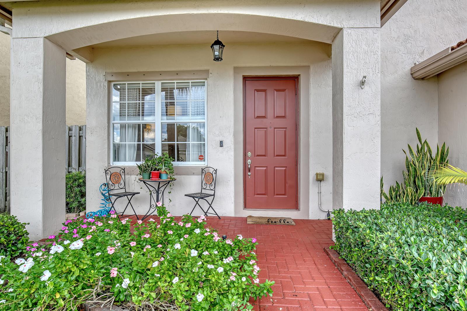 A front porch with a red door, brick flooring, a small bistro set, and landscaping — 10751 Oak Bend Way, Wellington FL 33414, WELLINGTON, FL