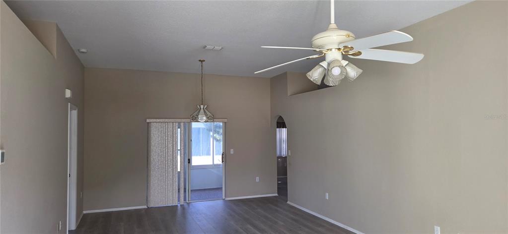 A living room with light brown walls, wood-look flooring, a ceiling fan, and sliding doors — 4224 AVANTI CIRCLE, NEW PORT RICHEY, FL