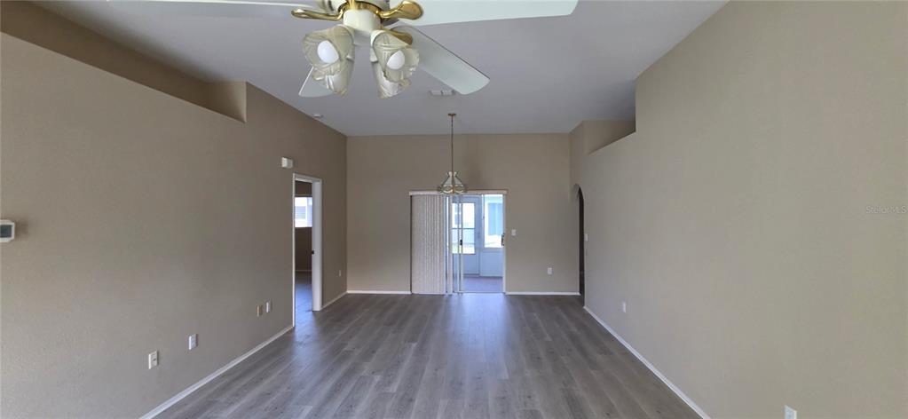An empty room features light-colored walls, wood-look flooring, a ceiling fan, and sliding glass doors — 4224 AVANTI CIRCLE, NEW PORT RICHEY, FL
