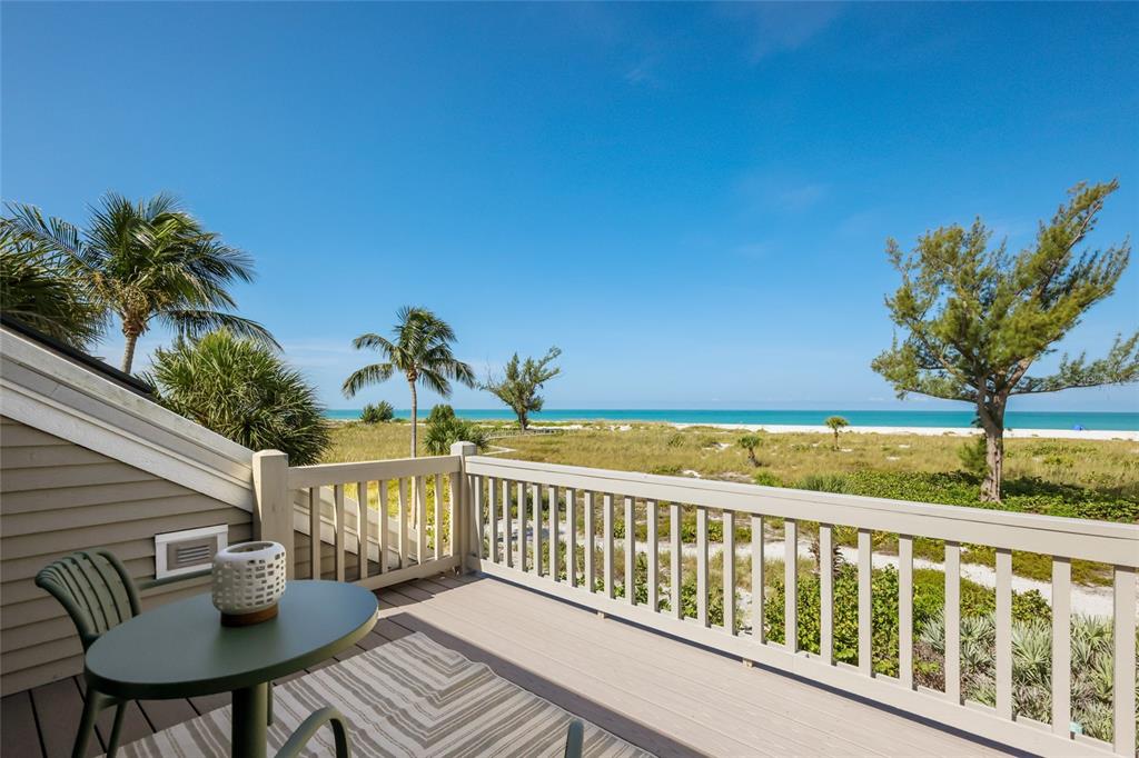 A wooden balcony with a small table and chairs overlooks a beach and the ocean — 17 SEAWATCH DRIVE, BOCA GRANDE, FL