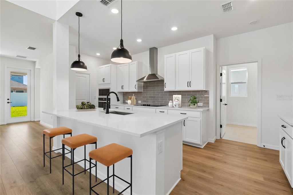 A modern kitchen features white cabinets, a quartz island with bar stools, and wood flooring — 15227 EASTLYN DRIVE, BRADENTON, FL