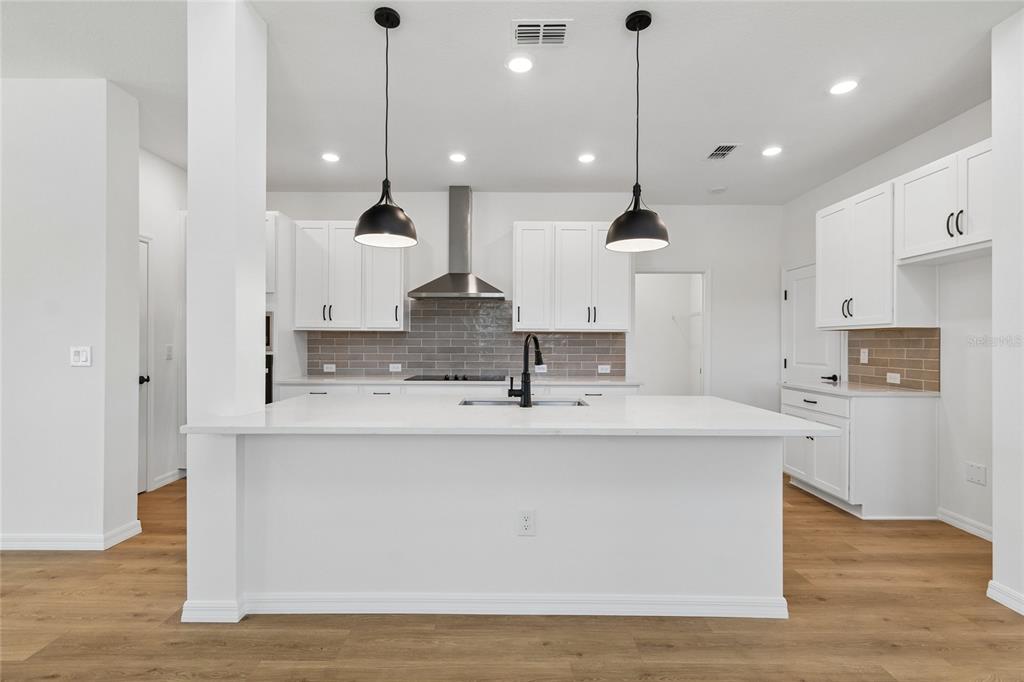 A modern kitchen features white cabinetry, a large quartz island, and a gray tile backsplash — 15227 EASTLYN DRIVE, BRADENTON, FL