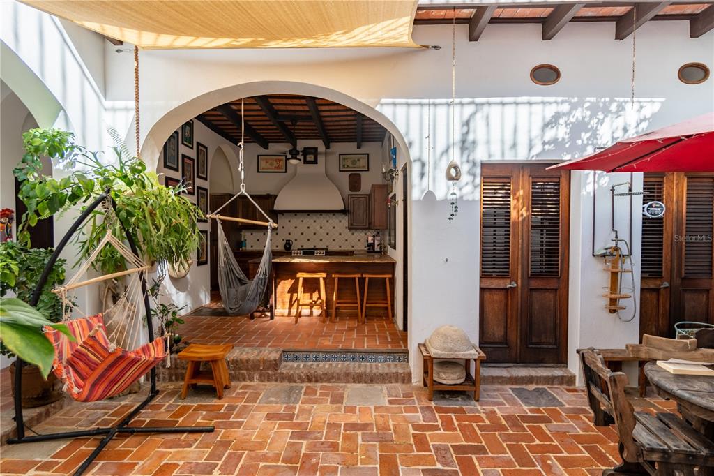 An outdoor patio with brick flooring, a hammock, and an arched entryway to a kitchen — 3 CRUZ, SAN JUAN, PR