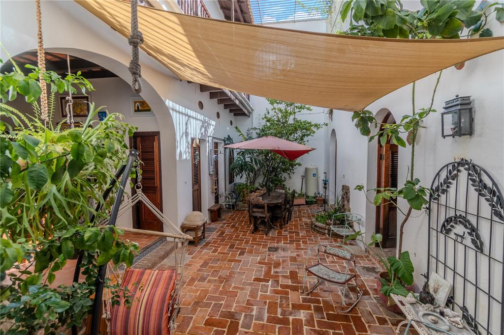 An outdoor courtyard features brick flooring, a shade sail, a dining set, and potted plants — 3 CRUZ, SAN JUAN, PR