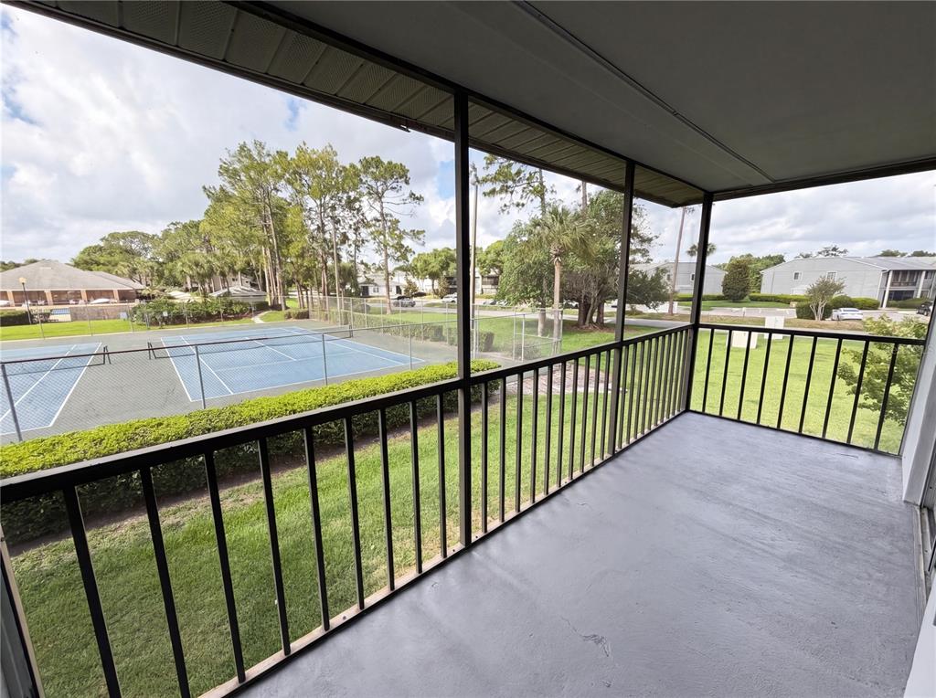 A screened-in balcony overlooks a tennis court and a grassy lawn with trees — 2749 OAK PARK WAY UNIT 203, ORLANDO, FL