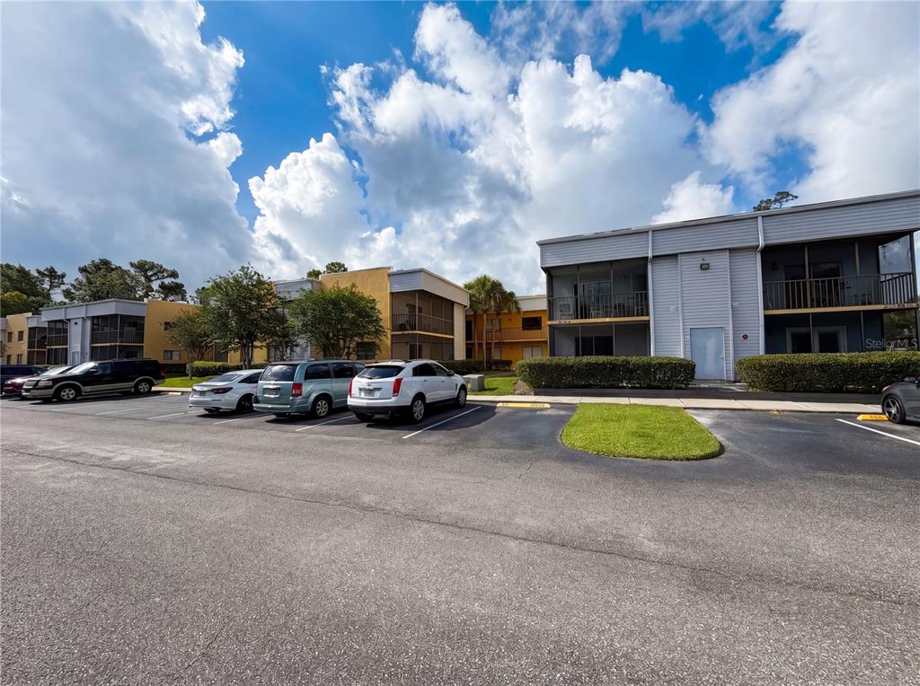 A parking lot sits in front of two-story apartment buildings under a cloudy blue sky — 2749 OAK PARK WAY UNIT 203, ORLANDO, FL