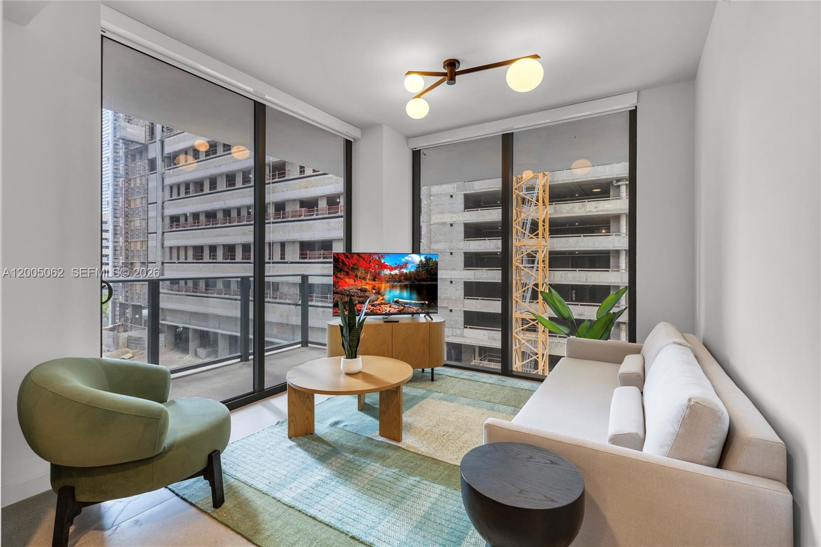A modern living room features a sofa, armchair, and floor-to-ceiling windows overlooking a construction site — 11 NE 6th St # 407, Miami FL 33132, MIAMI, FL