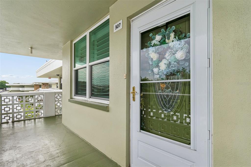 A white door with a floral wreath and a window sits on a green balcony — 4885 1ST ST NE UNIT 307, ST PETERSBURG, FL