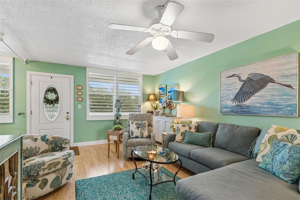 A living room features a blue sectional sofa, patterned armchair, ceiling fan, and coastal decor — 4885 1ST ST NE UNIT 307, ST PETERSBURG, FL