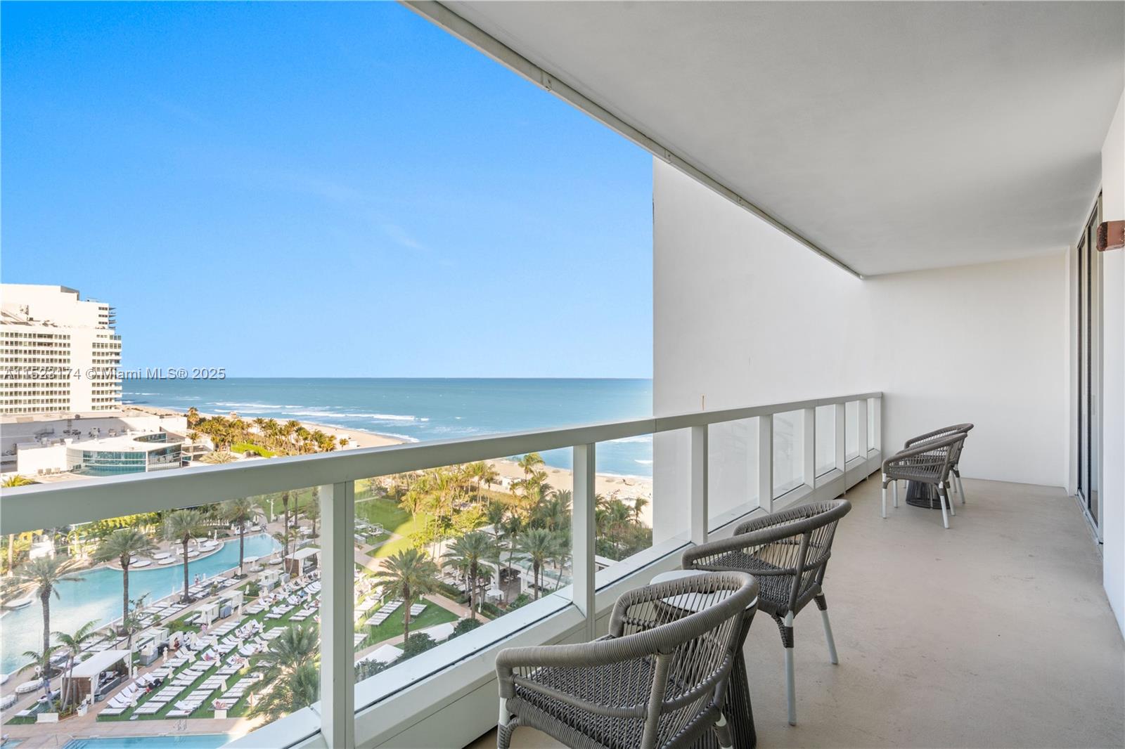 A balcony with gray chairs overlooks a beach, palm trees, and the ocean — 4391 COLLINS AV # 1007, Miami Beach FL 33140, MIAMI BEACH, FL